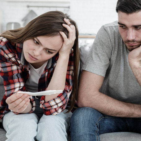 Young sad couple looks upset because of positive results of pregnancy test