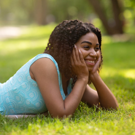 Attractive black lady in blue dress relaxing on grass at summer park